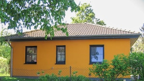 A yellow building with a tiled roof, three windows, and a chain-link fence in front. - Vacation cottage Bohne, Germany (Kenz-Küstrow)
