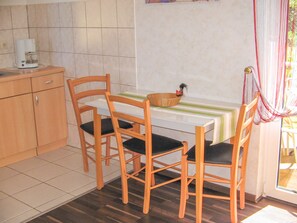 A small kitchen with a dining table, chairs, a coffee maker, and a basket with a rooster decoration. - Vacation cottage Bohne, Germany (Kenz-Küstrow)