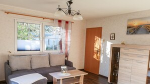 A living room with a sofa, a coffee table, a wooden cabinet, and a window with curtains. - Vacation cottage Bohne, Germany (Kenz-Küstrow)