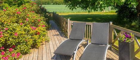 Una terraza de madera con dos sillones de mimbre y una jardinera con flores.