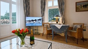 Un salon avec un téléviseur, une table en verre ornée d’un vase de fleurs et une vue sur la mer, visible à travers de grandes fenêtres.