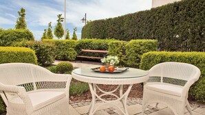 Un espace extérieur aménagé avec deux fauteuils en osier, une table en verre et un banc.