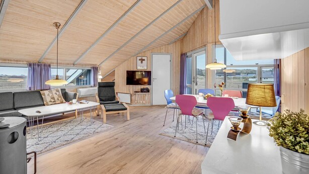 A spacious living area with a high ceiling, wooden walls, a dining table with colorful chairs, a sofa, and a TV. - Beautiful home in Ringkøbing with sauna (Ringkøbing)