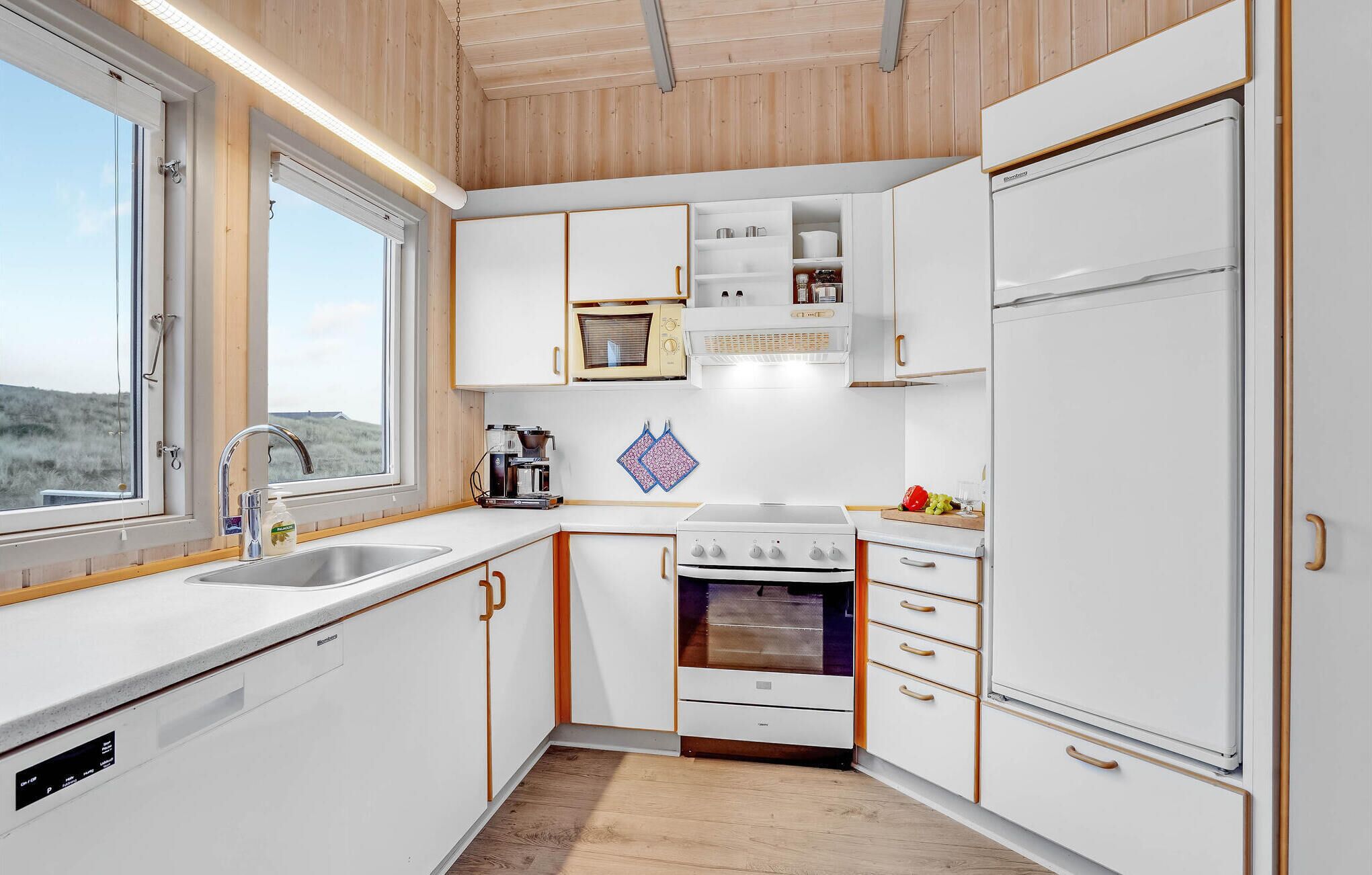 Uma cozinha compacta com armários brancos, forno embutido, micro-ondas e pia.