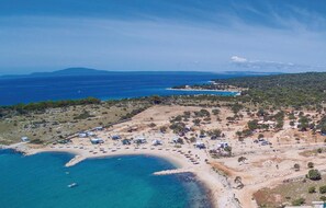 Enjoy a serene beachside retreat with umbrellas and tents lining the shore, surrounded by boats and hilly terrain.