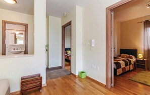 Hotellihuone, jossa on puulattia, kuviollinen päiväpeite sängyllä, yöpöytä lampun kanssa ja kylpyhuone, jossa on pesuallas ja peili.