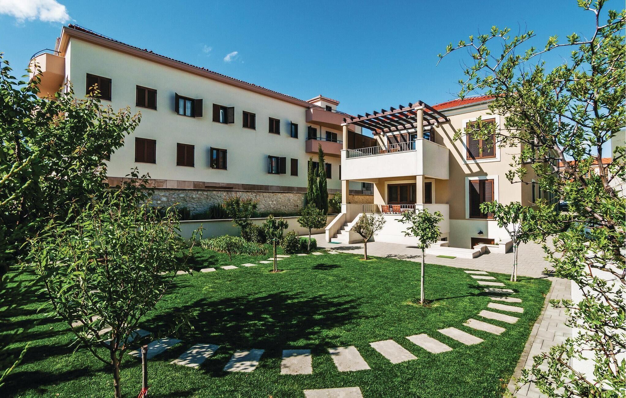 A courtyard with a well-maintained lawn, a stone pathway, and a two-story building with balconies.