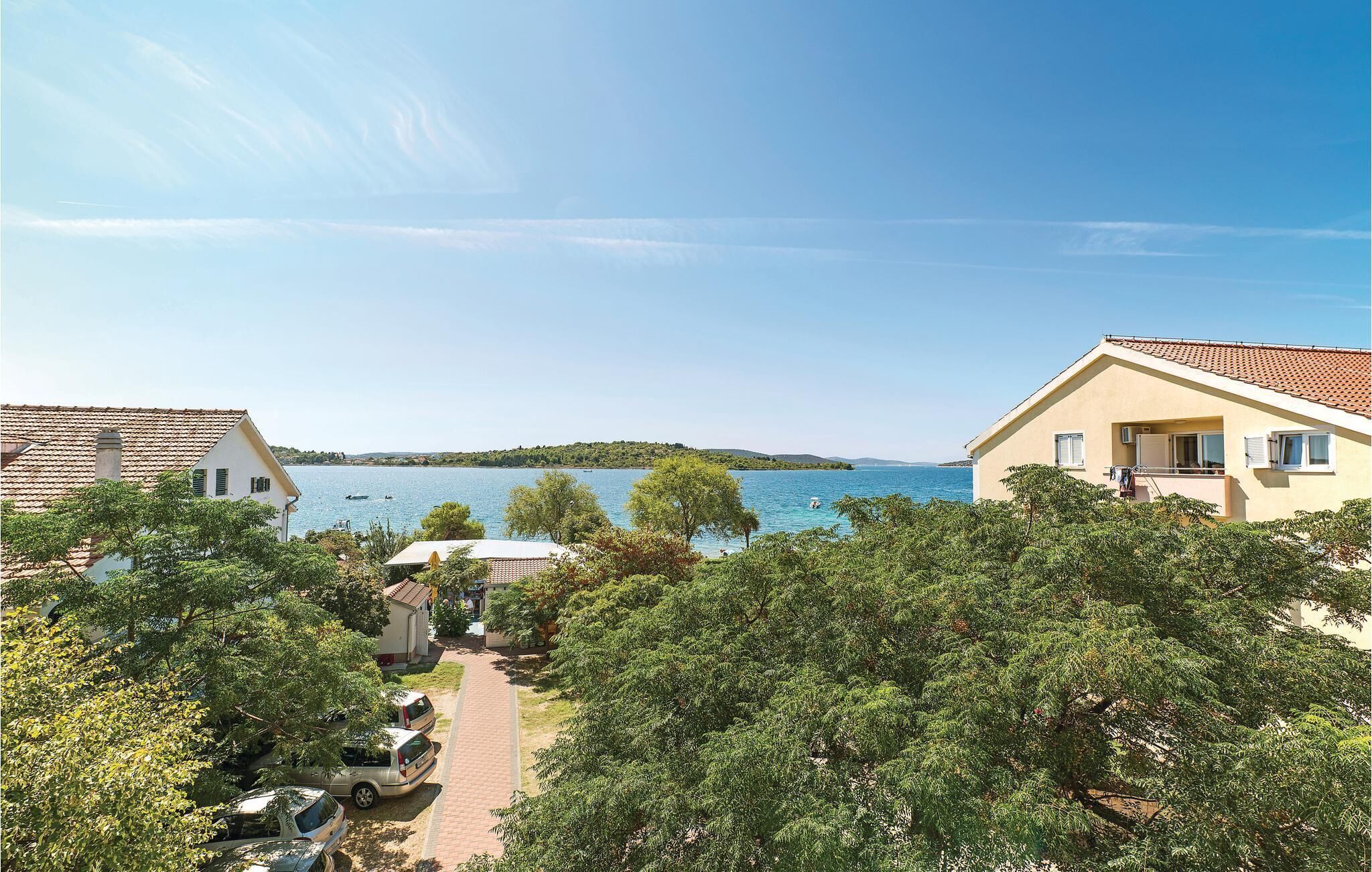 A coastal property with a paved pathway leading to a beach, surrounded by lush greenery and a clear view of the sea.