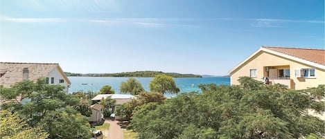 A coastal property with a paved pathway leading to a beach, surrounded by lush greenery and a clear view of the sea.