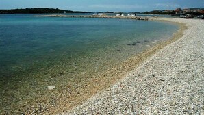 Una playa de guijarros con agua cristalina, un bote y una costa lejana con edificios.