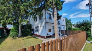 A two-story residential building with a fenced backyard, a patio with outdoor furniture, and a wooden fence.
