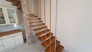 A spiral staircase with wooden steps and bamboo railings, leading to a landing area with a stone pillar.