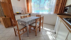 A compact kitchen with a dining area, featuring a tiled floor, wooden furniture, and a window with sheer curtains.