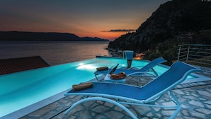 A poolside area with lounge chairs and a table, overlooking a body of water and hills during sunset. - Awesome apartment in Duba (Duba)