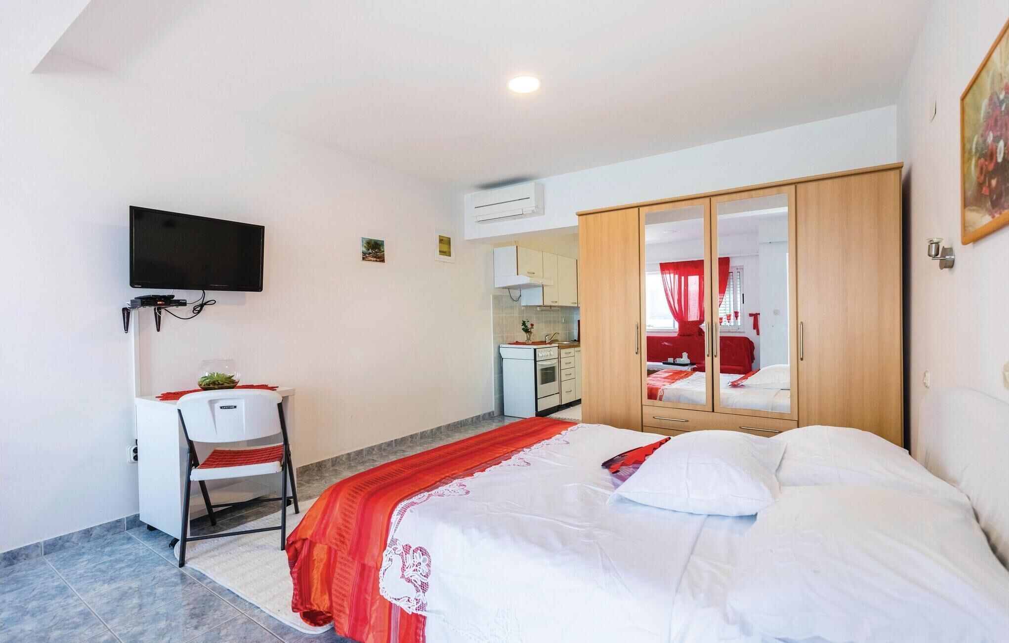 A bedroom with a bed, a desk with a chair, a TV mounted on the wall, and a wardrobe.