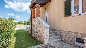 Una casa con una scala in pietra che conduce a una porta, una piscina sullo sfondo e un prato curato.
