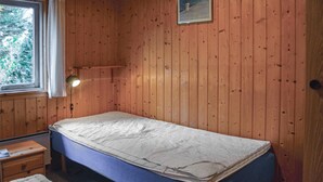 A small, single-bed room with wooden walls, a bedside lamp, a small table, and a window with a view of trees. - 4 bedroom stunning home in Thisted (Thisted)
