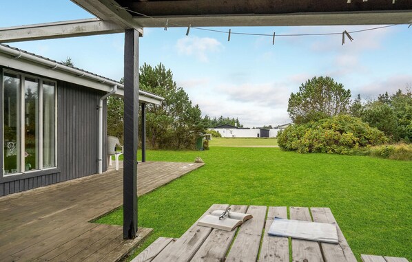 Un patio abrité avec une terrasse en bois, une pelouse verdoyante et, au loin, une vue sur un immeuble d’habitation.