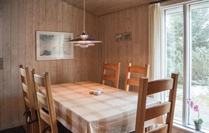 A dining area with a wooden table, chairs, a pendant light, and a window with a view of trees.