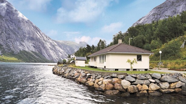 Ein Haus am See mit einer Steinmauer und Bergen im Hintergrund.