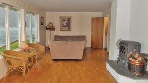 Ein Wohnzimmer mit einer Couch, Korbstühlen, einem Kamin und Blick auf das Wasser durch große Fenster.