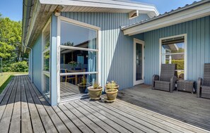 A modern house with a wooden deck, a glass door leading to a dining area, and outdoor furniture.