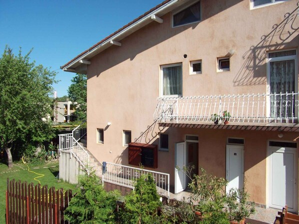 A two-story building with a balcony, a wooden fence, and a garden area.
