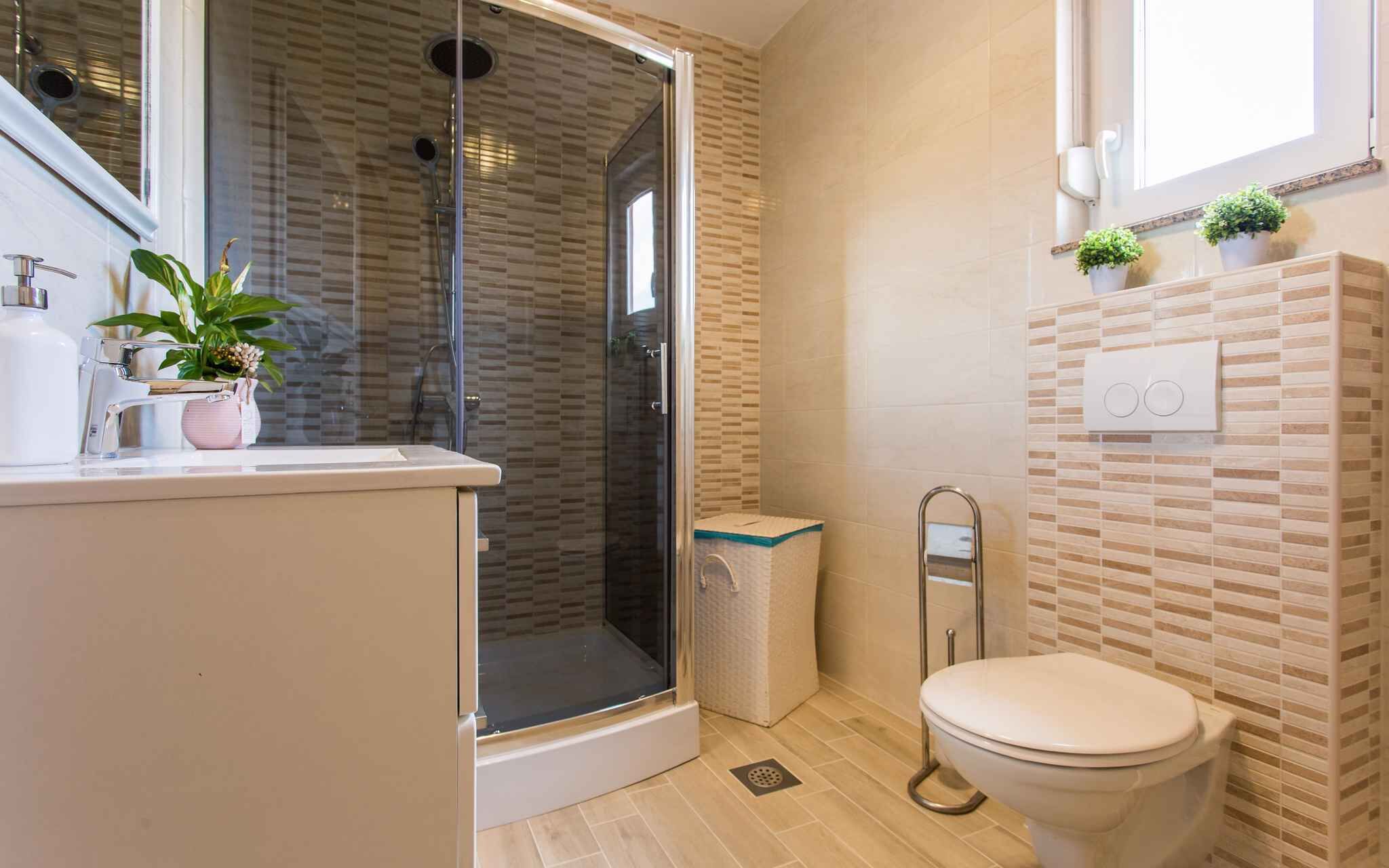 Een badkamer met een douchecabine van glas, een toilet, een wastafel met spiegel en een raam met planten.
