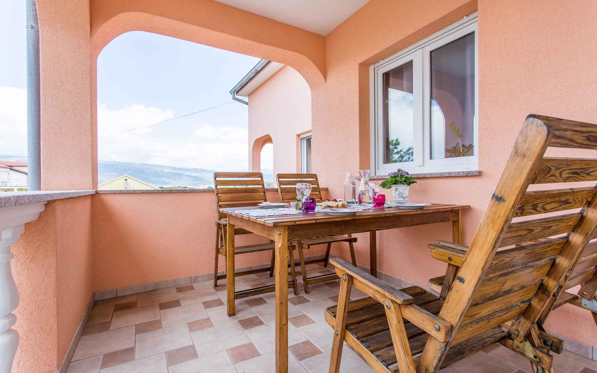 A balcony with a wooden table and chairs, a window with a view, and a potted plant.