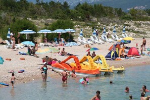 A beach with sun loungers, umbrellas, and inflatable water toys. - Holiday apartment with balcony and air conditioning (Šilo)