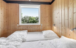 Cozy retreat with a large window offering a view of lush greenery and a comfortable bed with a bedside table and lamp.