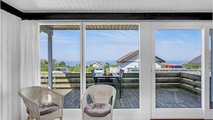 Een balkon met twee rieten stoelen en een tafel, uitkijkend op een houten terras en een uitzicht op zee.