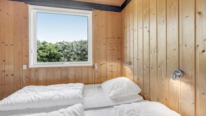 Een houten kamer met een bed, een raam en uitzicht op bomen.