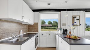 Een moderne keuken met witte kasten, een roestvrijstalen spoelbak en een raam met uitzicht op een huis en tuin.
