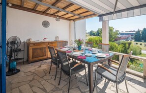 Eine überdachte Terrasse mit Esstisch, Stühlen, einer Uhr und Blick auf die Umgebung.