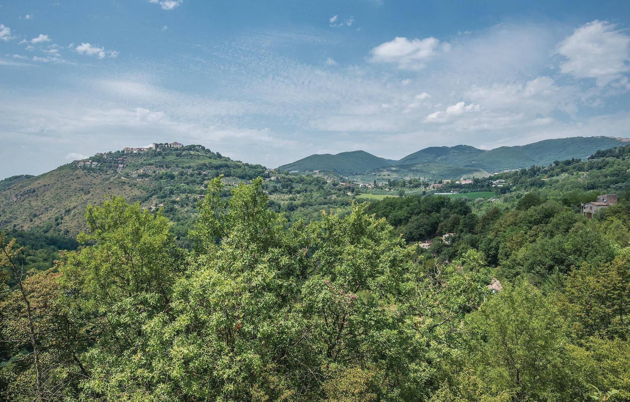 A mountainous landscape with scattered buildings, dense green foliage, and a clear sky.