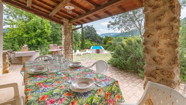 Un espace extérieur aménagé pour les repas, avec une pergola en bois, une piscine et une vue sur la verdure et les collines.