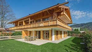 Eine zweistöckige Holzchalet mit Balkon, einer Terrasse mit Gartenmöbeln und einem gepflegten Rasen.