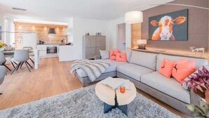Ein modernes Wohnzimmer mit einem grauen Sofa, einem Couchtisch und einer Küche im Hintergrund.