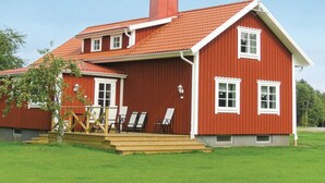 A red wooden house with a sloped roof, a chimney, and a small porch with chairs.