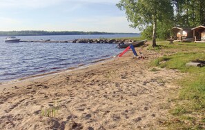 A sandy beach with a boat docked on the water, a small dock, and a row of cabins in the background.