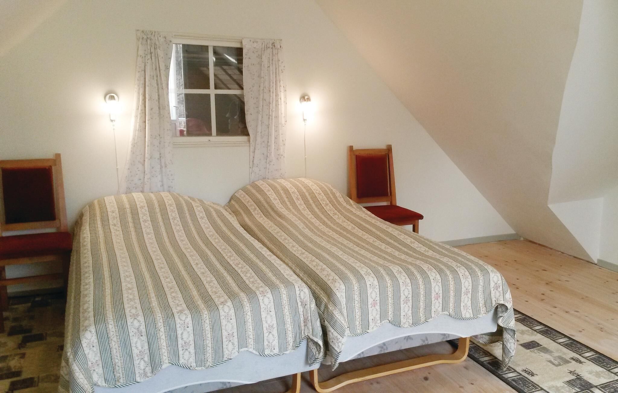 Une chambre avec deux lits simples, une fenêtre avec des rideaux, une chaise en bois et une petite table.