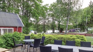 An outdoor seating area with wicker chairs and a table, surrounded by greenery and a red building. - 4 bedroom nice home in Eringsboda (Eringsboda)