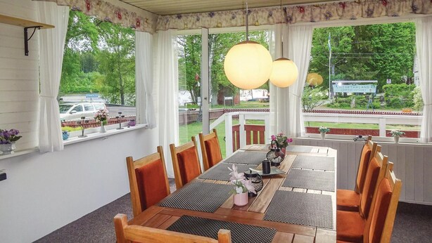 A dining area with a long table, chairs, and large windows with curtains. - 4 bedroom nice home in Eringsboda (Eringsboda)
