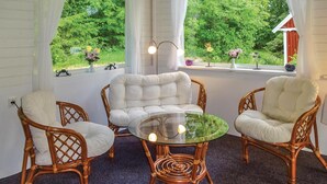 A cozy seating area with wicker chairs and a glass table, overlooking a lush garden through large windows. - 4 bedroom nice home in Eringsboda (Eringsboda)