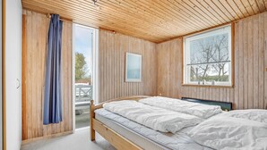 A bedroom with two beds, wooden walls, a large window, and a door leading outside.