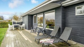A covered patio with outdoor furniture, a wooden deck, and a view of a residential building with large windows.