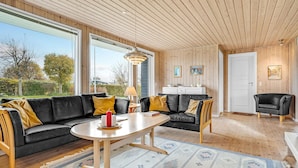 A modern living room with a black leather sofa, a wooden dining table, and a large window providing a view of the outdoors.