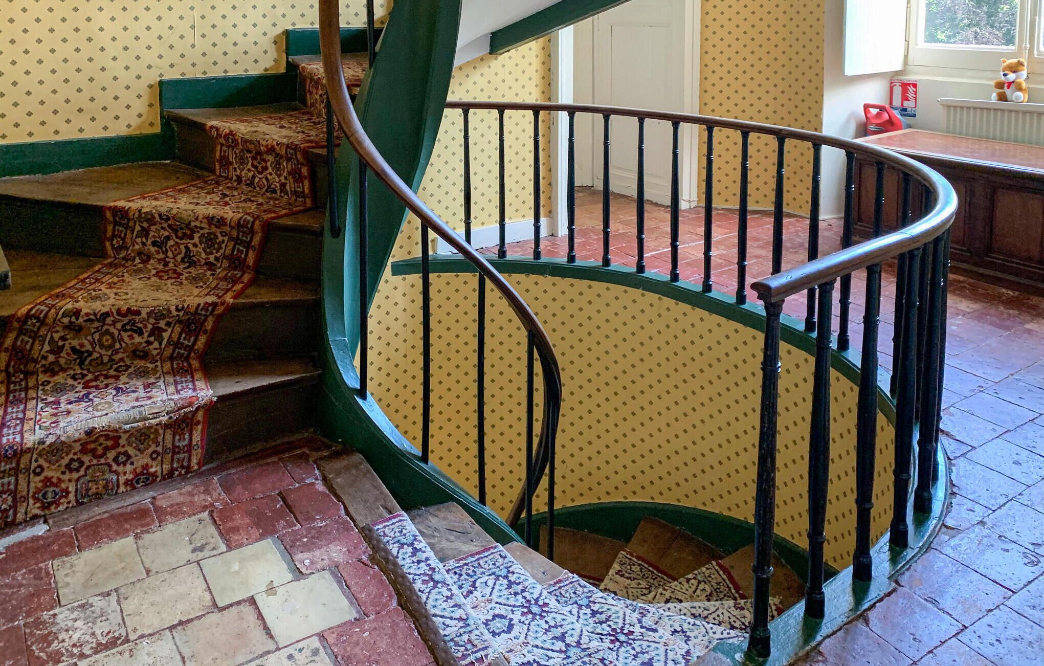 A spiral staircase with a patterned carpet and a green railing.
