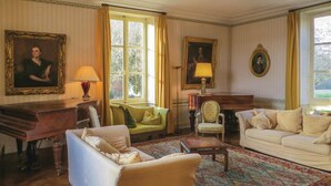 Une pièce au décor traditionnel, avec un piano, deux canapés, un tapis à motifs et des œuvres d’art encadrées accrochées aux murs.